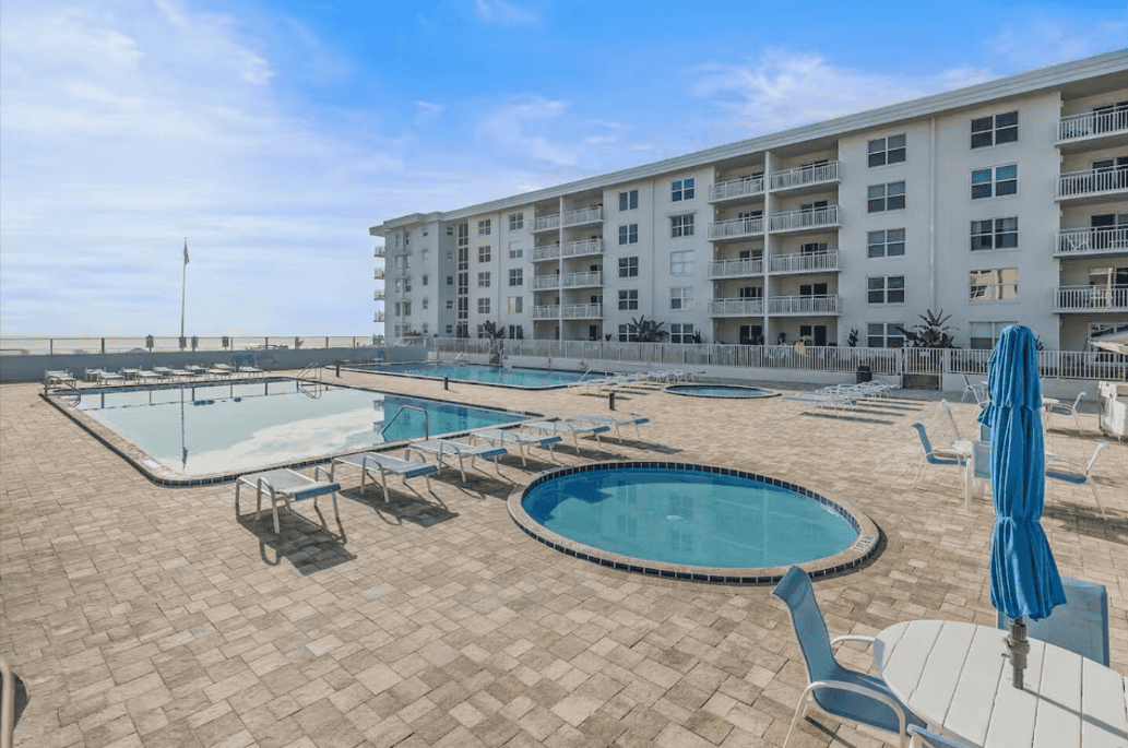 Oceanfront condo pool deck with two large swimming pools, two circular kiddie pools, lounge chairs, and beach access at Sea Coast Gardens II in New Smyrna Beach.