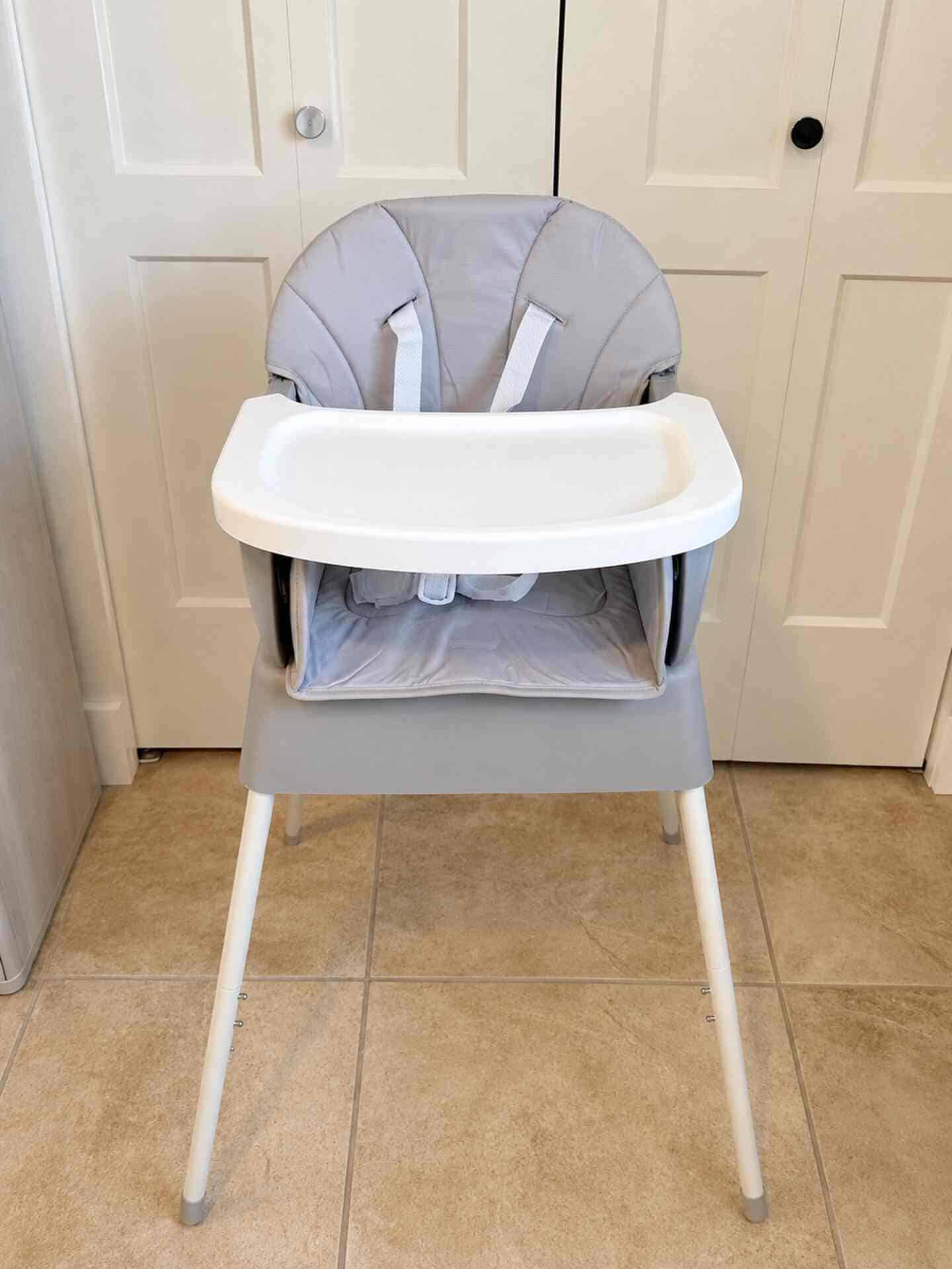 Gray baby high chair with safety harness and tray for feeding.