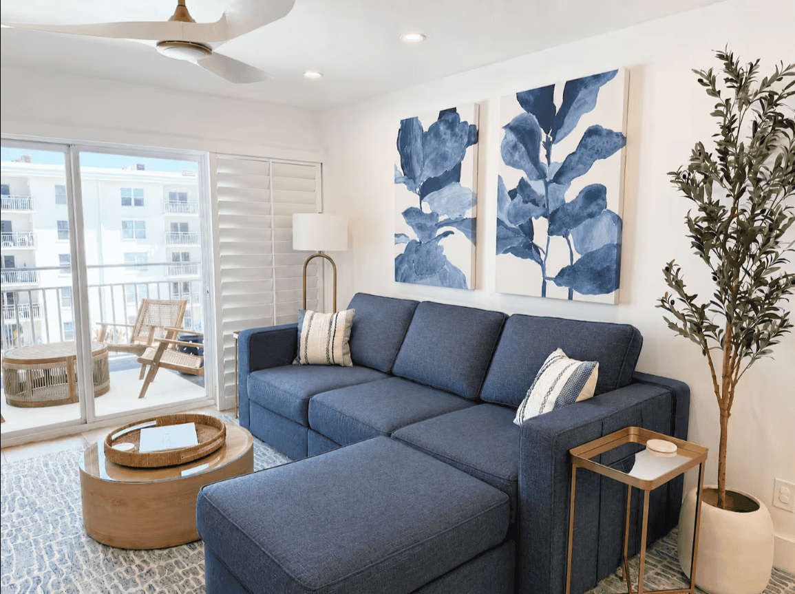 Bright coastal living room with blue sectional and private balcony at Salt & Vine Beach House in New Smyrna Beach, Florida